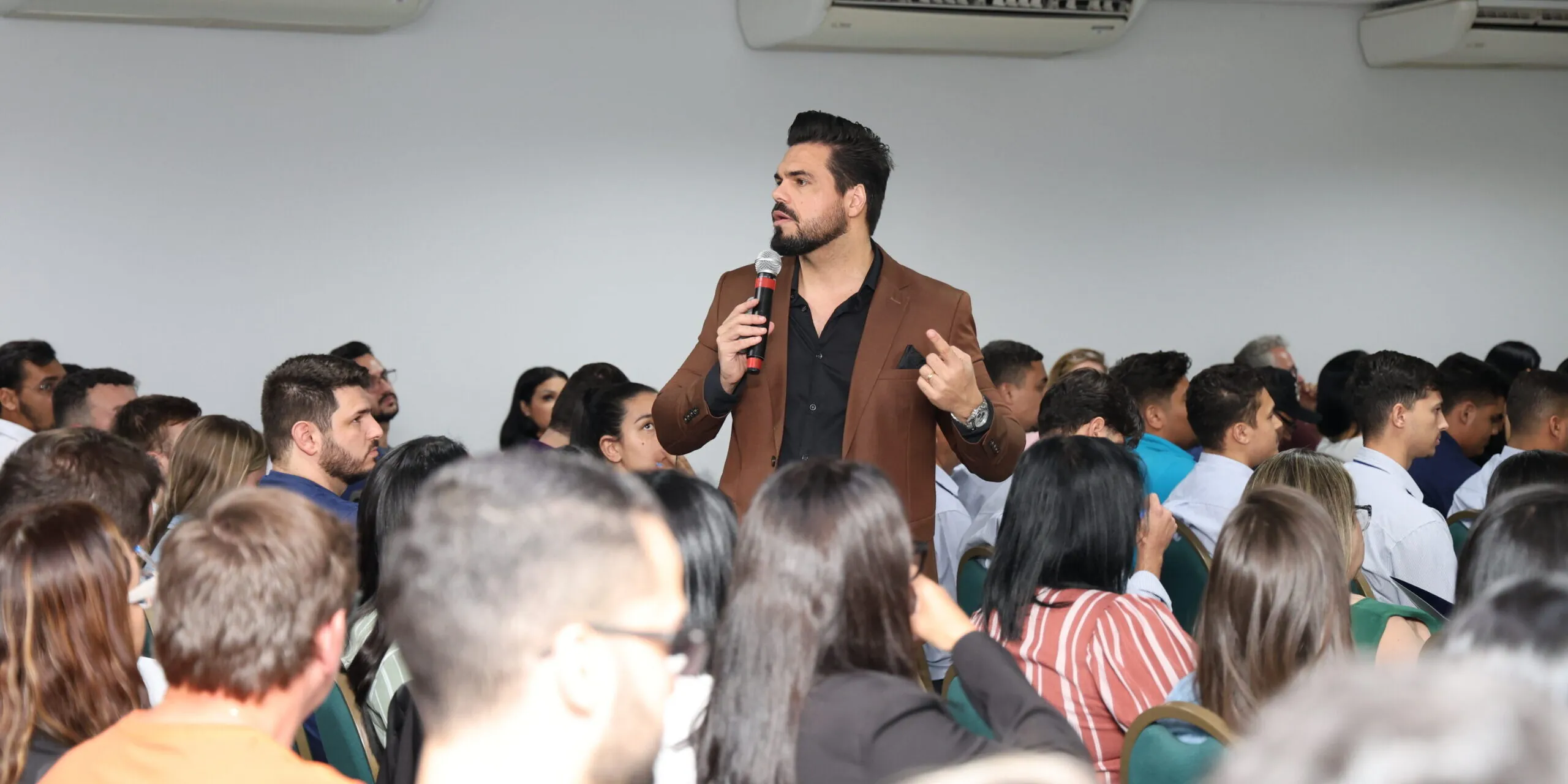Janderson Santos em pé diante de sala lotada durante treinamento de vendas